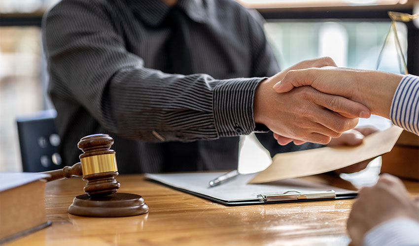 Two people shaking hands with documents and a gavel on the desk