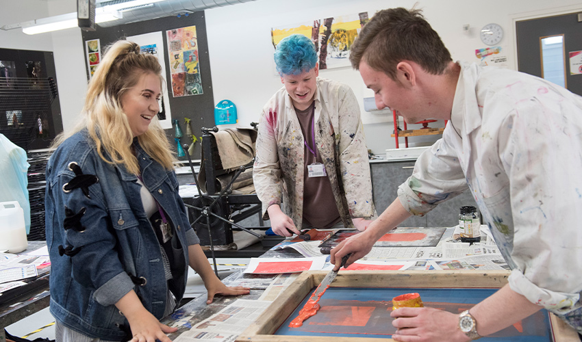 Image of a paintbrush being dipped into a palette of paints, with a journal on the side.