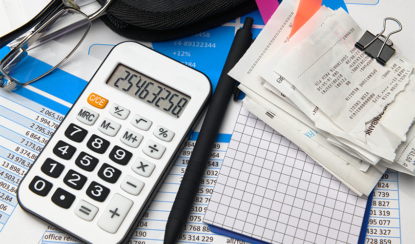 A calculator, receipts, pen, glasses, and financial documents arranged on a desk.