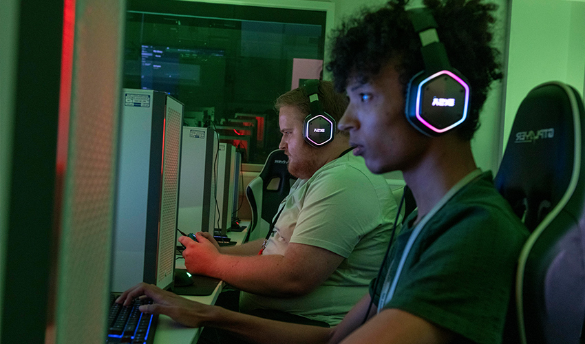 An image of students playing games on pcs, with headphones on.