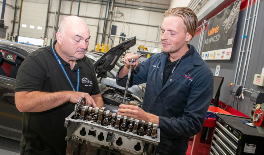 Motor vehicle apprentice with his tutor working on an engine