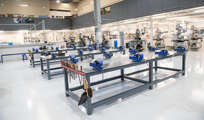 Technical workshops with multiple workbenches equipped with vices and milling machines for hands-on engineering training.