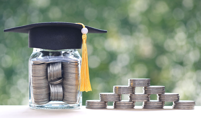Jar of money with a graduation hat on top, next to stacked piles of coins
