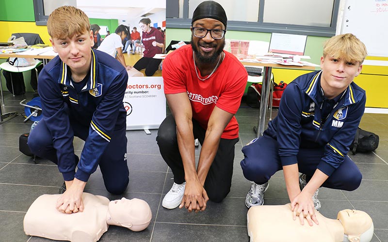 Students Oscar Suter l and Max Meehan r practice CPR with the support of Street Doctor Jesse Anim
