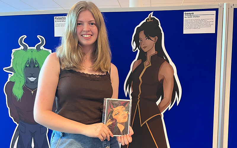 Sadie Shelton holds a print of her original character, Saaya, which she created as part of her digital media practice course. Her project combined digital illustration with creative writing.