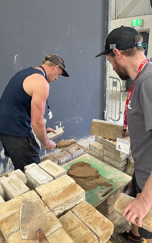 Dale in action practicing the brick laying with Bradley assisting
