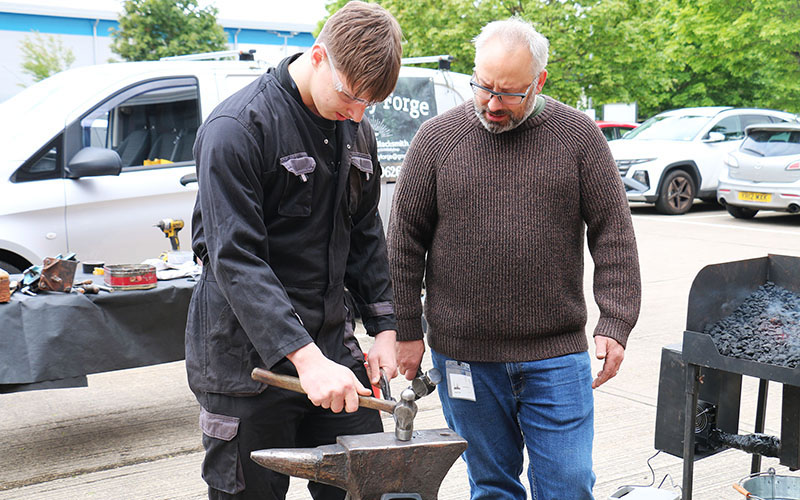 Level 1 Fabrication and Welding student Niks Gadiskis shapes the metal watched by Graham