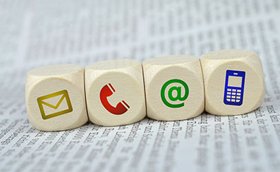 photo of four dice sitting on a newspaper, each dice has an image of an at symbol, a letter, a phone and a mobile phone