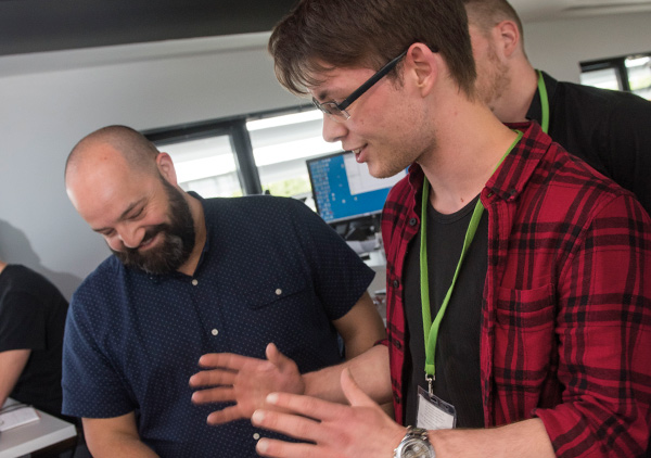 Image of a group of men stood having a discussion whilst looking over some paperwork.