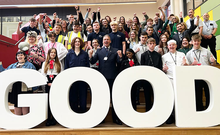 Group photo of a college principal stood in front of a large group of students stood behind large white letters that spell GOOD.