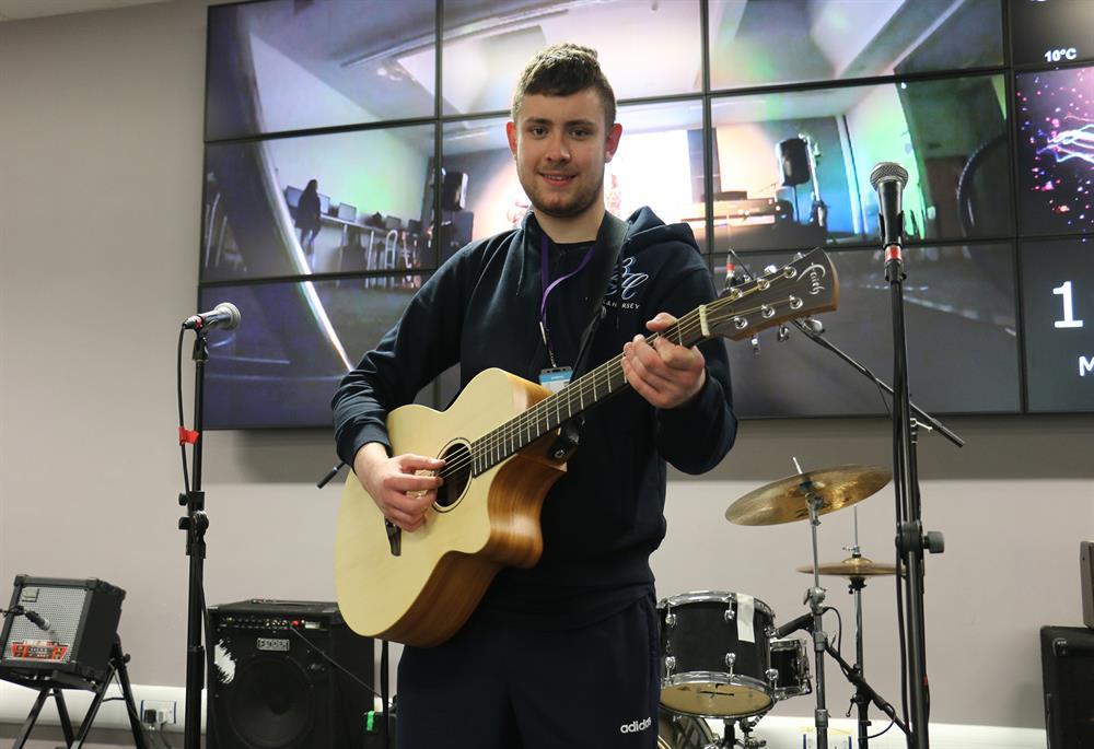Ashley performing on stage at the College’s Create venue, proudly sporting his brand-new acoustic guitar.