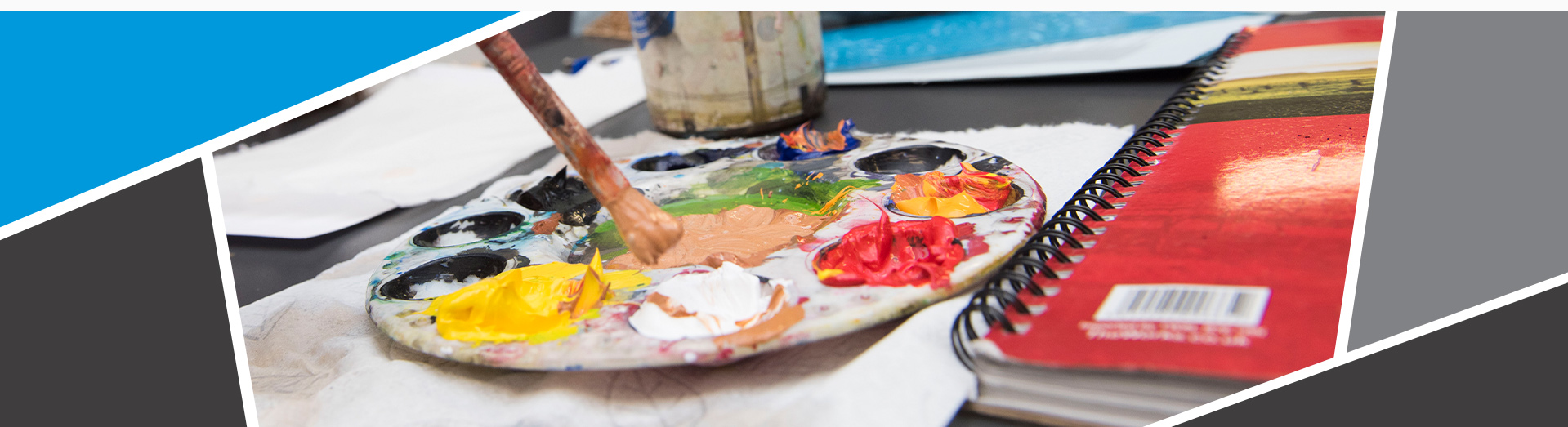 Image of a paintbrush being dipped into a palette of paints, with a journal on the side.