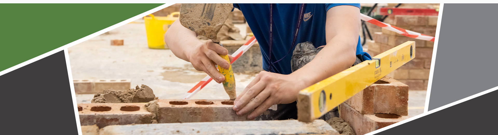 An image of a student building a brick wall, holding a trowel tapping a brick into place.