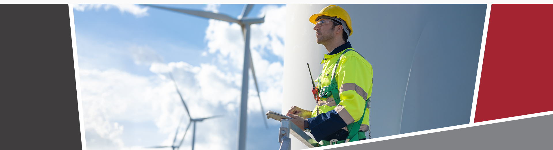 A worker in a high-visibility jacket and yellow hard hat stands against the backdrop of wind turbines, holding a clipboard,