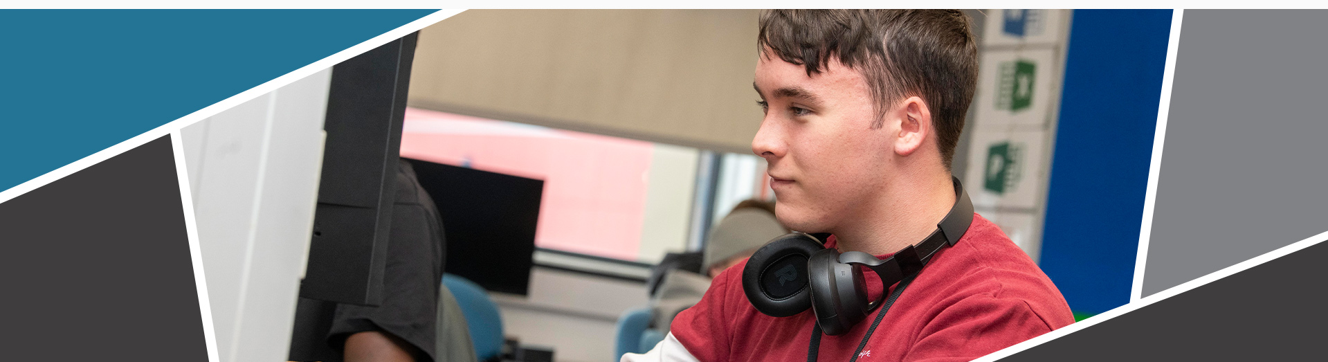 A banner of a student using a computer, smiling with headphones around his neck.