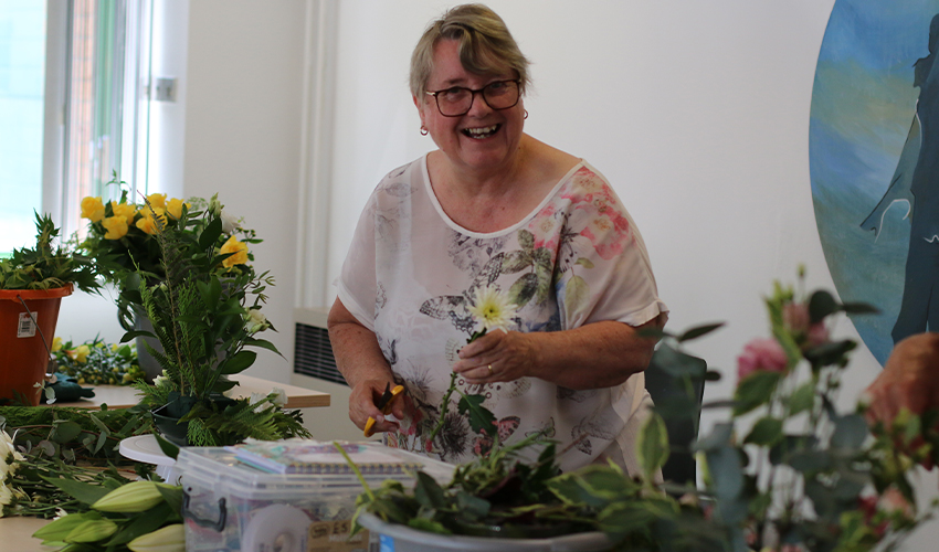 An image of a woman enjoying flower arranging, smiling at the camera.