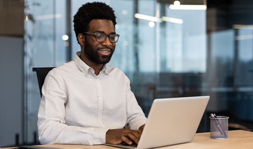 A male sat at a desk using a laptop.