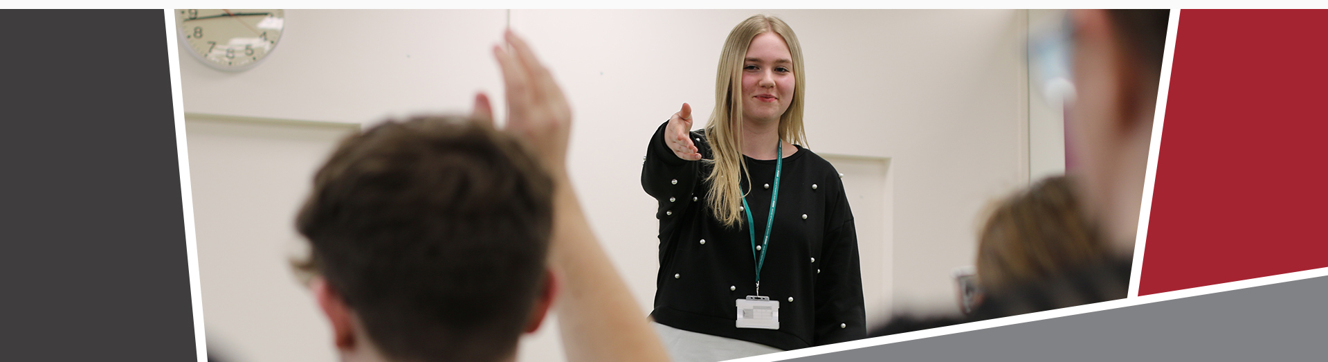 An image of a young student smiling and pointing to a member of the audience with their hand up. 
