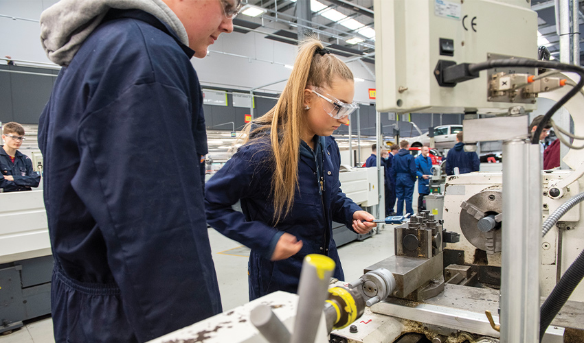 an image of a girl using a lathe with a boy stood beside her observing.